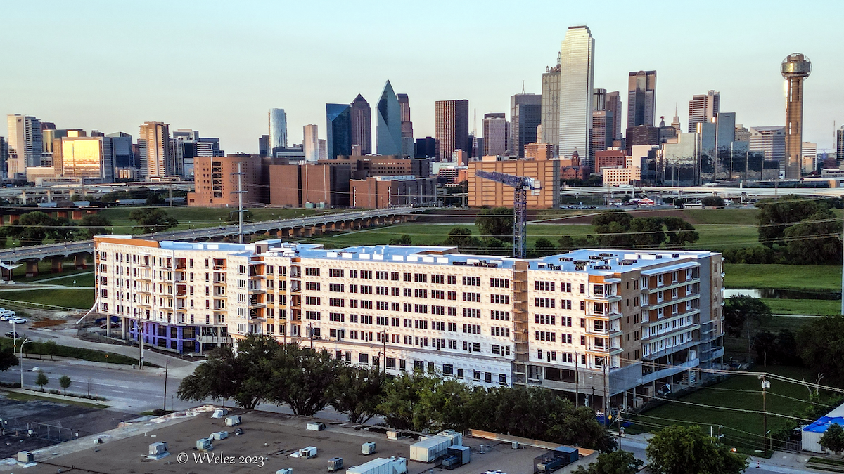 A large residential and commercial edification, with downtown Dallas in the background.